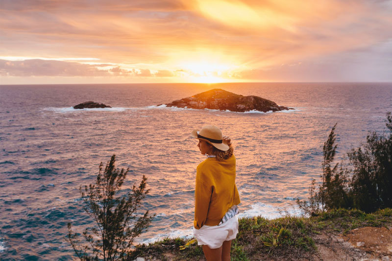 Woman at Edge of Cliff Overlooking Ocean at Sunset